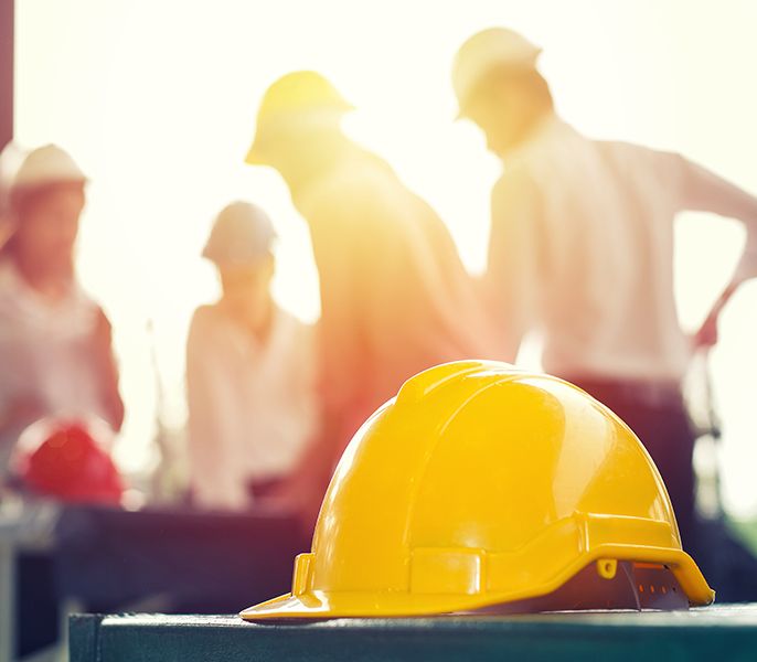 Yellow hard hat sitting on a table with workers with hard hats blurred in background