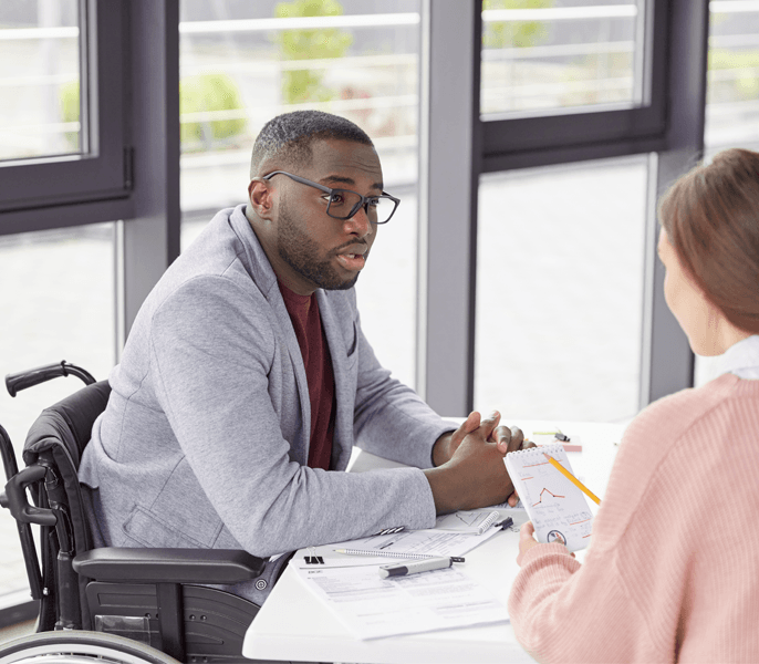 Man in wheelchair having a discussion with a colleague in office setting